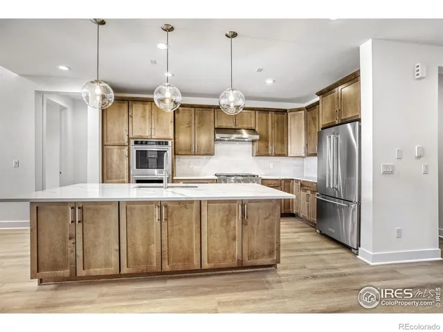 a kitchen with stainless steel appliances kitchen island granite countertop a refrigerator a sink dishwasher a stove and a wooden cabinets