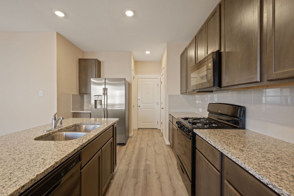 602 Knopper Street, Unit B Pflugerville, TX 78660 - Photo 6 of 26 Kitchen with black appliances, light wood-type flooring, light stone countertops, decorative backsplash, and recessed lighting