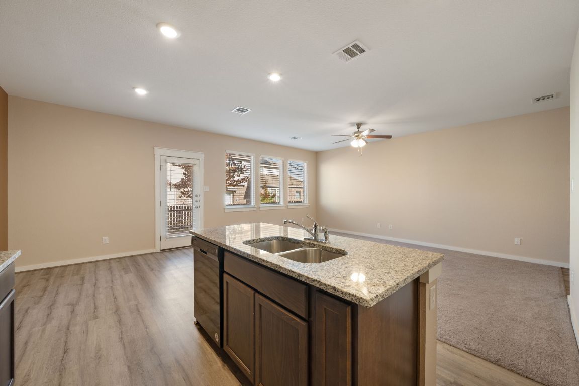 602 Knopper Street, Unit B Pflugerville, TX 78660 - Photo 26 of 26 Kitchen featuring open floor plan, dark brown cabinetry, light stone counters, black dishwasher, and an island with sink