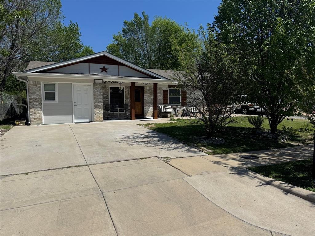 View of front of property featuring a porch, brick siding, concrete driveway, and a front lawn