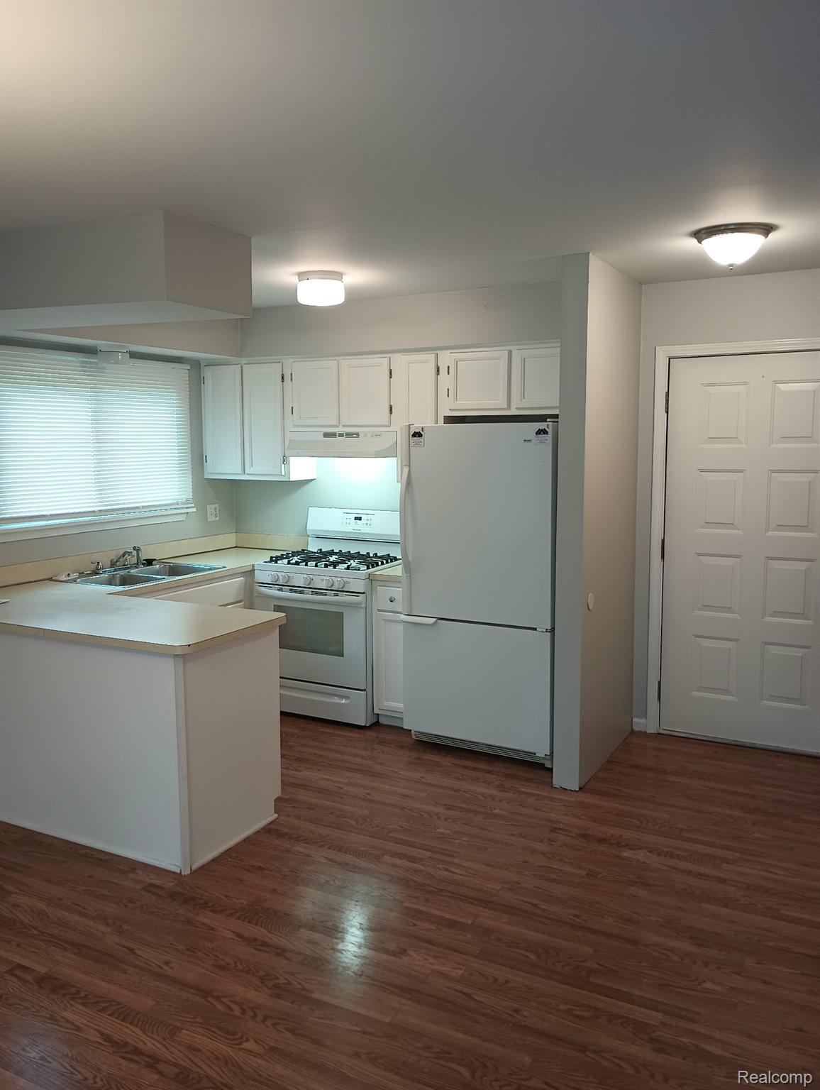 Kitchen featuring white cabinetry, white appliances, wood-finish flooring, and a peninsula with countertop