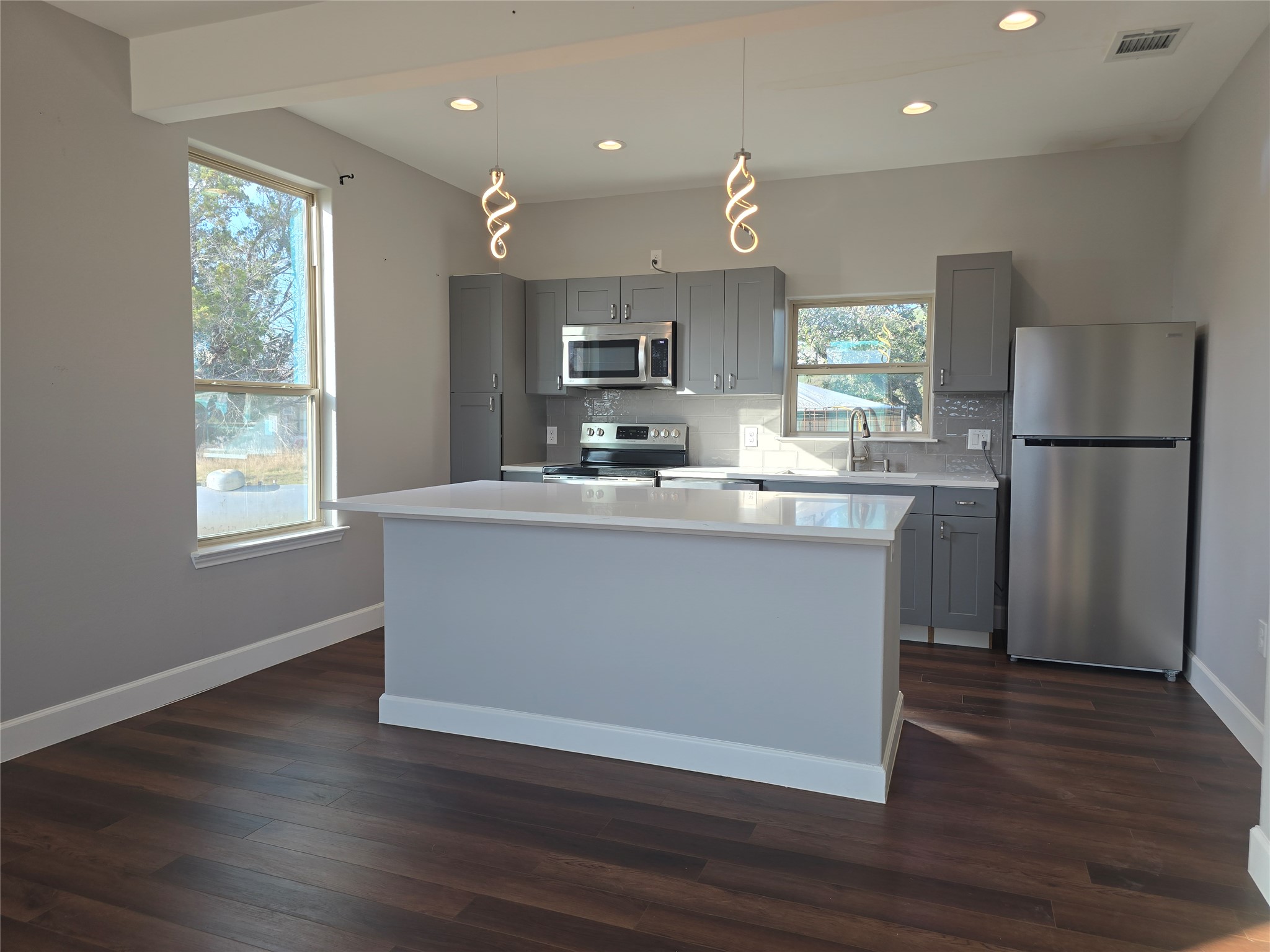 304 Spring Street Burnet, TX 78611 - Photo 9 of 11 Kitchen featuring gray cabinets, stainless steel appliances, a kitchen island, backsplash, and dark wood finished floors