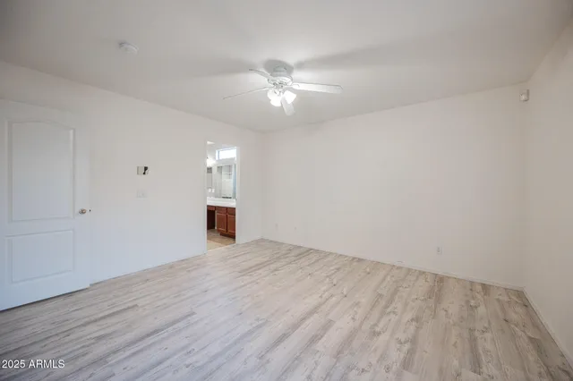 a view of an empty room with wooden floor and a ceiling fan