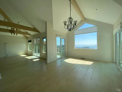 a view of an empty room with chandelier fan and wooden floor