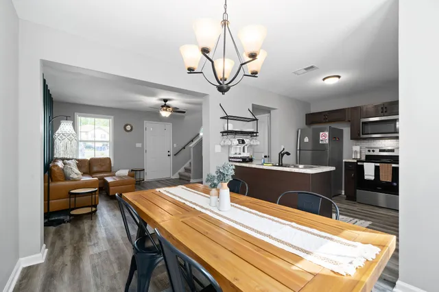 a room with stainless steel appliances kitchen island granite countertop a refrigerator a sink dishwasher a dining table and chairs with wooden floor