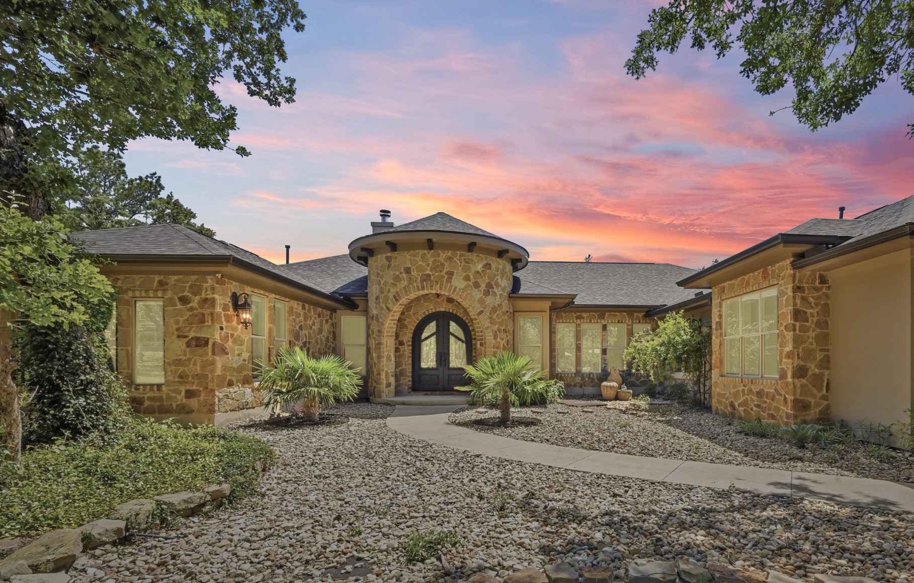 387 Corral Road Smithville, TX 78957 - Photo 10 of 40 Stone facade residence featuring a circular turret entry with an arched double door, a paved walkway, and low-maintenance rock landscaping