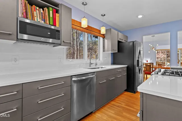 a kitchen with stainless steel appliances granite countertop a stove a sink a refrigerator white cabinets and wooden floor