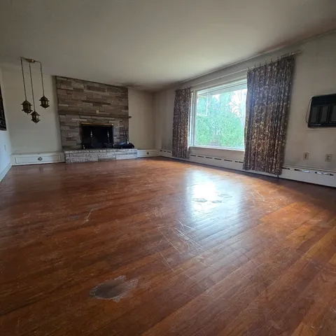 an empty room with wooden floor fireplace and windows