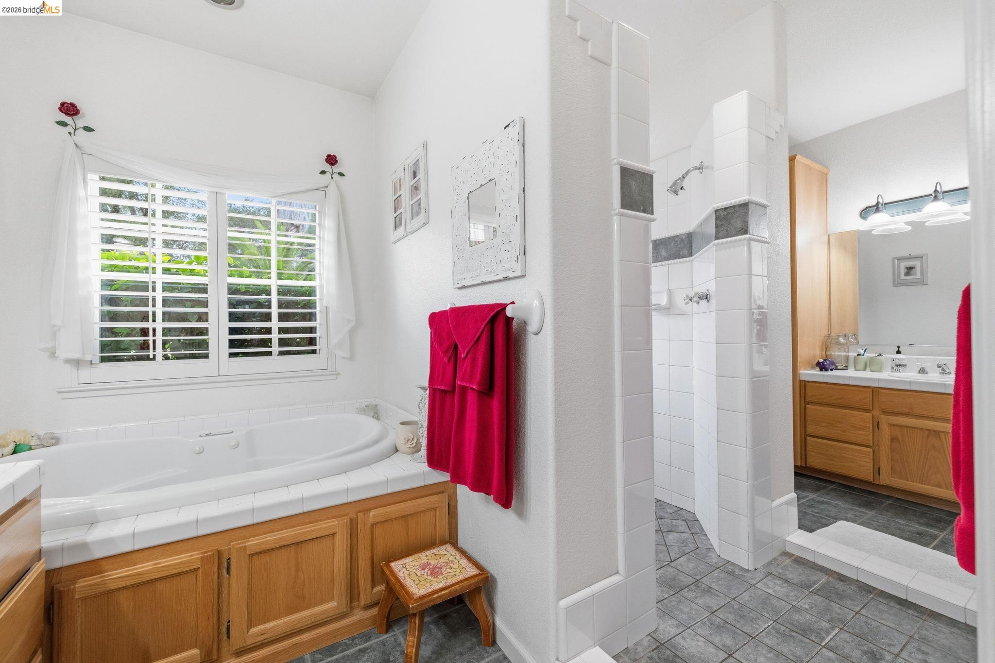 18450 Lambert Lake Road Sonora, CA 95370 - Photo 25 of 87 Soaking tub with white tile surround, integrated wood cabinetry, and a window featuring plantation shutters