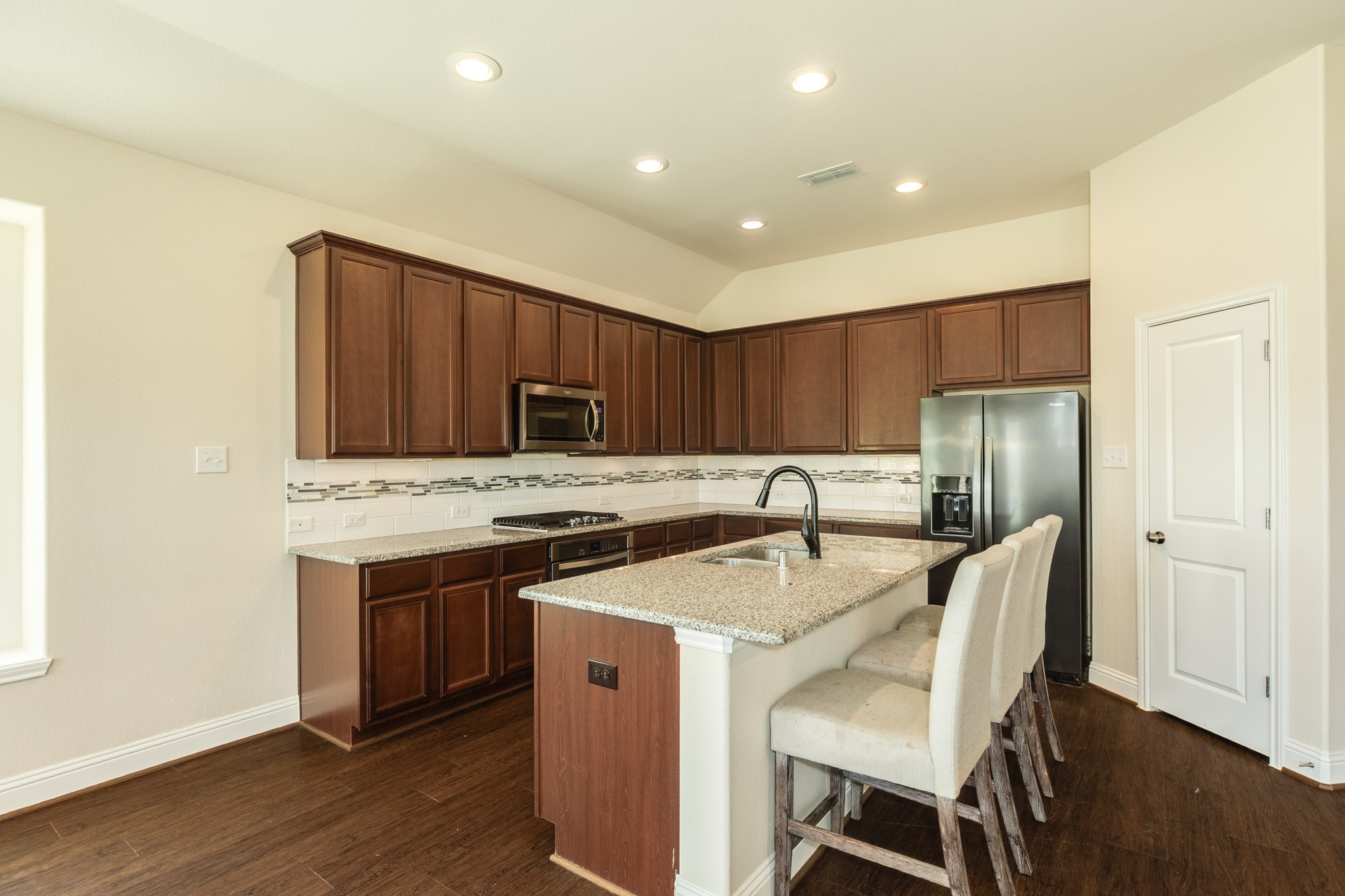 3519 Bay Drive Rosharon, TX 77583 - Photo 15 of 49 Modern kitchen featuring spacious granite countertops that serve as an ideal breakfast bar. To the right, a dedicated pantry door provides convenient access for storage. The space is further enhanced by elegant recessed lighting, creating a bright and inviting atmosphere.