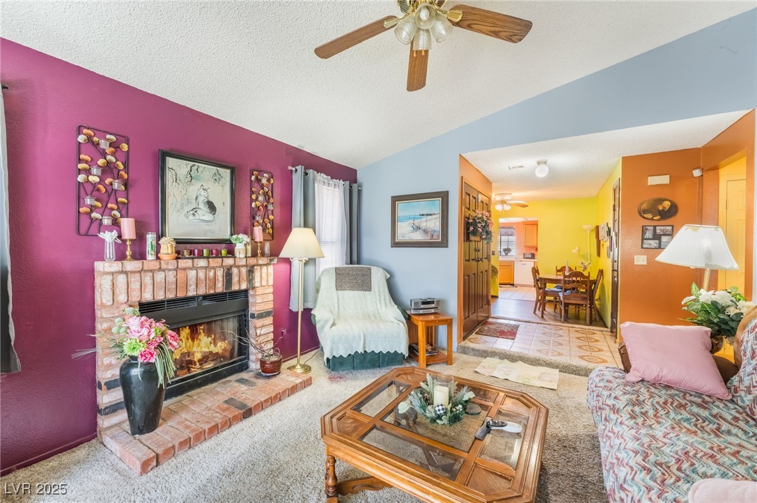6513 Deadwood Road Las Vegas, NV 89108 - Photo 11 of 34 Carpeted living area with a textured ceiling, vaulted ceiling, a brick fireplace, and ceiling fan