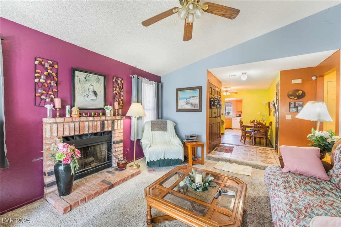 6513 Deadwood Road Las Vegas, NV 89108 - Photo 12 of 34 Carpeted living area with lofted ceiling, a textured ceiling, a brick fireplace, and ceiling fan