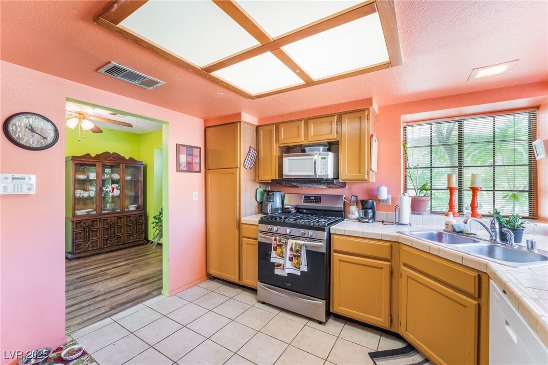 6513 Deadwood Road Las Vegas, NV 89108 - Photo 17 of 34 Kitchen with white appliances, light tile patterned floors, a textured ceiling, a ceiling fan, and tile counters