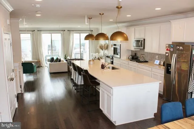 a open kitchen with stainless steel appliances granite countertop a refrigerator a sink dishwasher a dining table and chairs with wooden floor