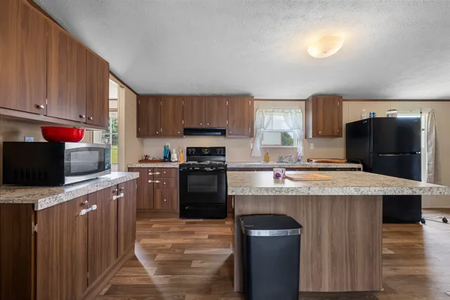 a kitchen with kitchen island granite countertop a stove top oven a sink dishwasher and a refrigerator with wooden cabinets