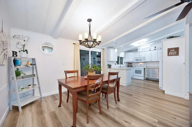 a large white kitchen with lots of white cabinets a sink dishwasher a dining table and chairs with wooden floor