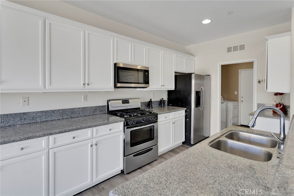 14245 Purple Canyon Road Adelanto, CA 92301 - Photo 12 of 38 a kitchen with granite countertop a sink a stove a microwave a refrigerator a counter space and cabinets