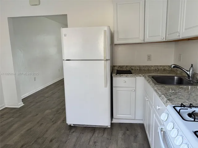 a kitchen with granite countertop a refrigerator sink and white cabinets