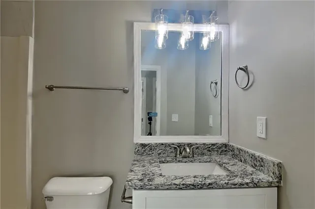 a bathroom with a granite countertop sink a toilet and mirror