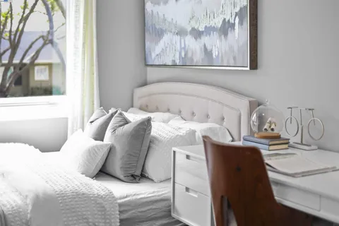 a bedroom with a bed a table and a large mirror next to a window