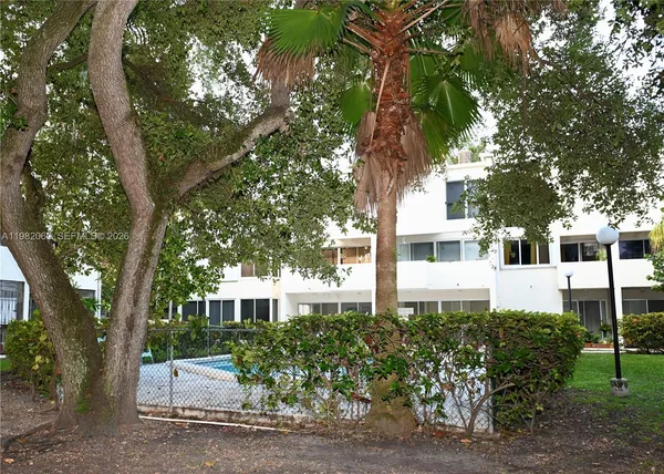 a view of a white house with a large tree and plants