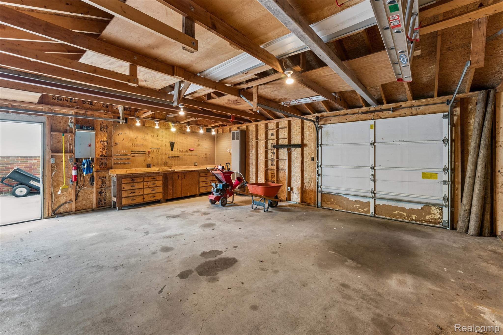 422 East Road Holly, MI 48442 - Photo 41 of 51 Spacious garage featuring exposed wood beam ceiling, concrete flooring, a built-in workbench with storage, wall-mounted utility panel, and a roll-up garage door