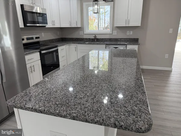 a kitchen with stainless steel appliances granite countertop a refrigerator a sink dishwasher a oven and a kitchen island with wooden floor