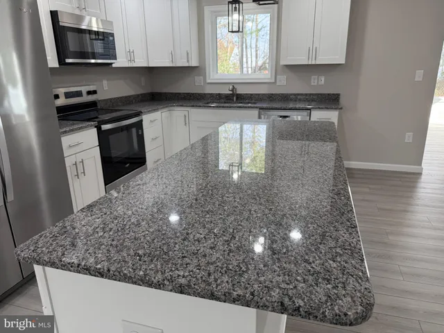 a kitchen with stainless steel appliances granite countertop a refrigerator a sink dishwasher a oven and a kitchen island with wooden floor