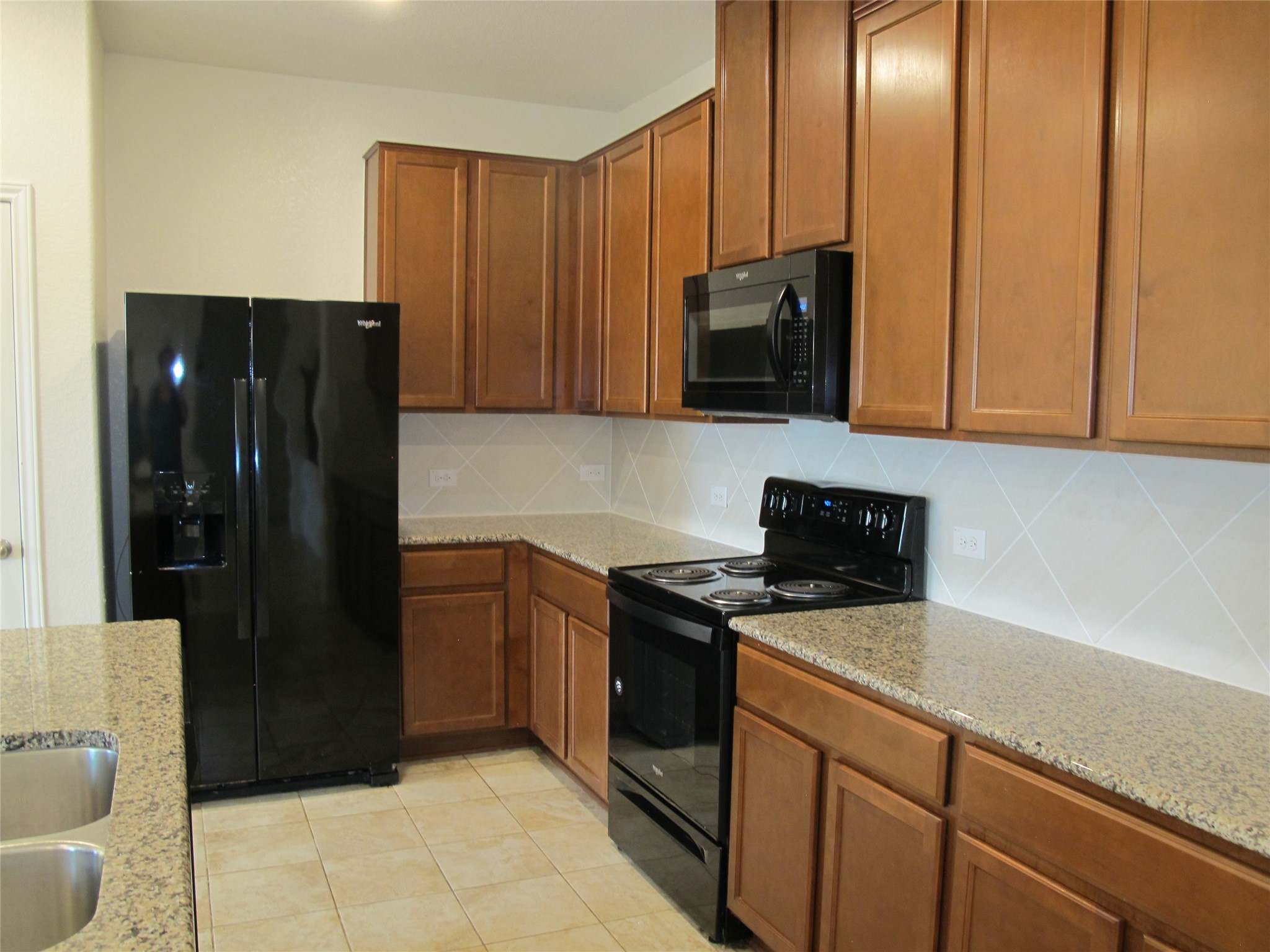 7820 Big Wind Way Austin, TX 78724 - Photo 13 of 37 Kitchen with black appliances, light stone counters, decorative backsplash, and brown cabinets