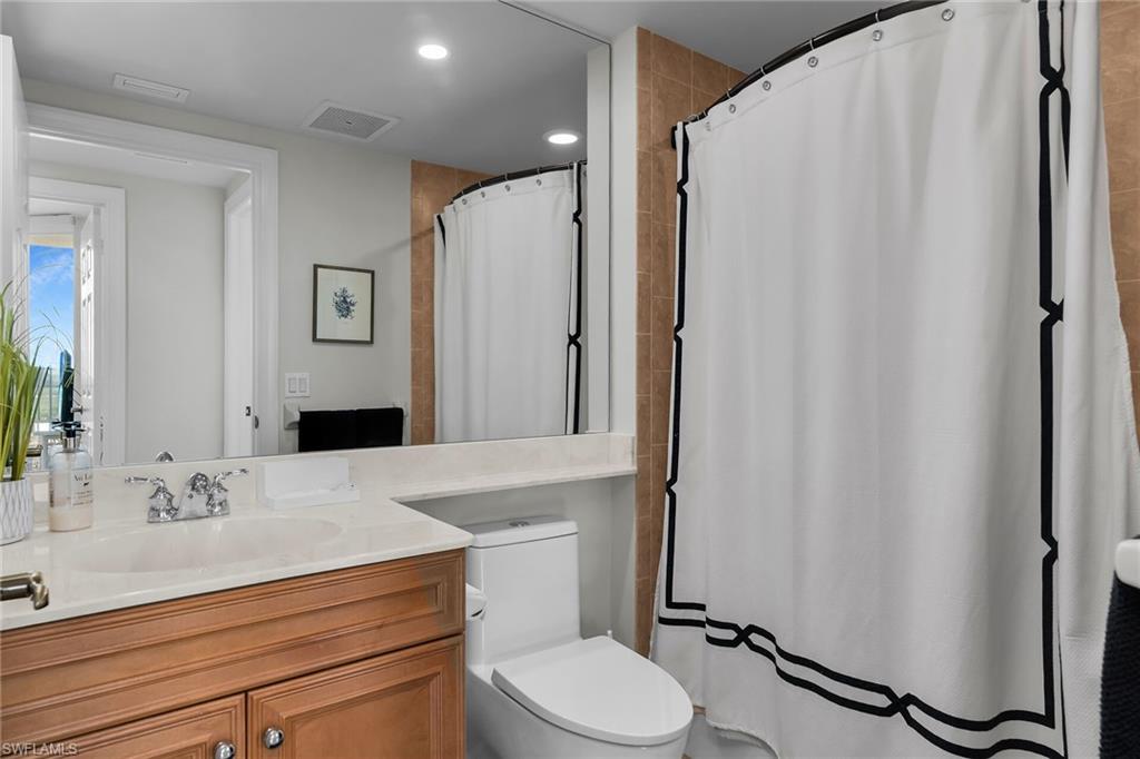 1065 Borghese Lane, Unit 1003 Naples, FL 34114 - Photo 23 of 35 a bathroom with a sink a toilet a mirror and shower curtain