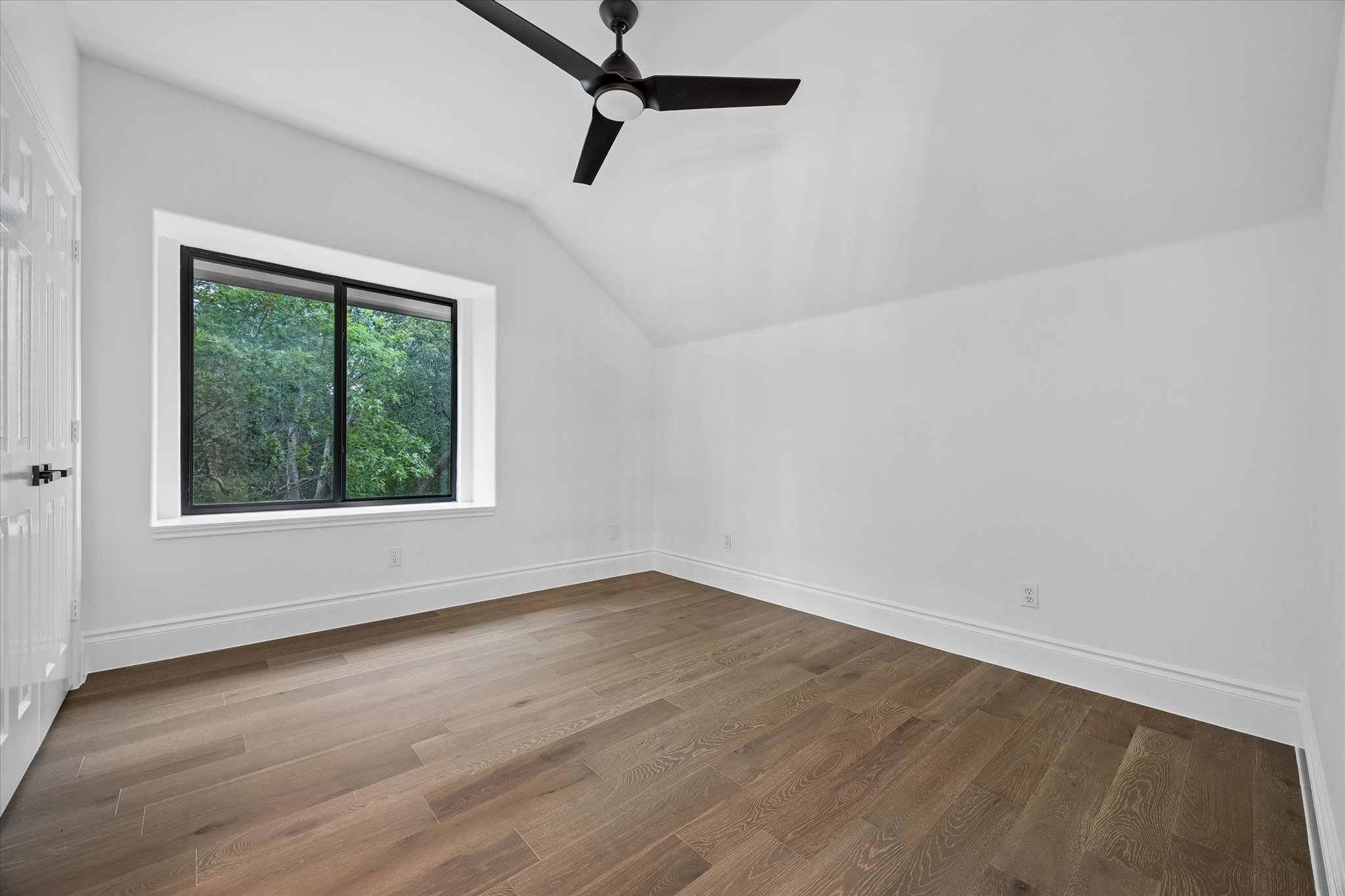 3719 Bee Creek Road Spicewood, TX 78669 - Photo 23 of 40 A well-lit bedroom with vaulted ceilings, a window offering views of mature trees, and elegant hardwood flooring.