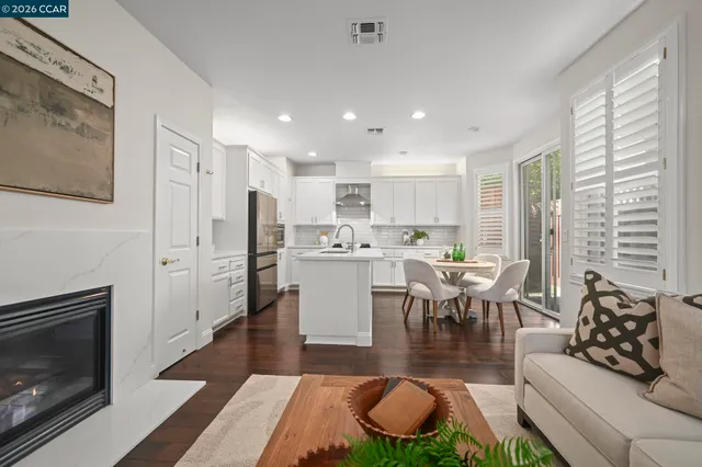 a living room with stainless steel appliances furniture wooden floor and a kitchen view