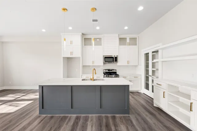 a large white kitchen with stainless steel appliances granite countertop a stove a sink dishwasher and a refrigerator with wooden floor