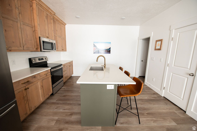 384 Ropelato Drive Nibley, UT 84321 - Photo 6 of 25 Kitchen featuring a breakfast bar area, stainless steel appliances, a kitchen island with sink, decorative backsplash, and dark wood-style floors
