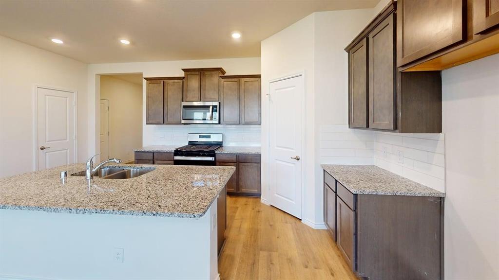 1306 Colonial Bluff Lane Princeton, TX 75407 - Photo 9 of 27 Kitchen featuring an expansive island with a stainless steel undermount sink, granite countertops, wood-finish flooring, a subway tile backsplash, and dark wood cabinetry