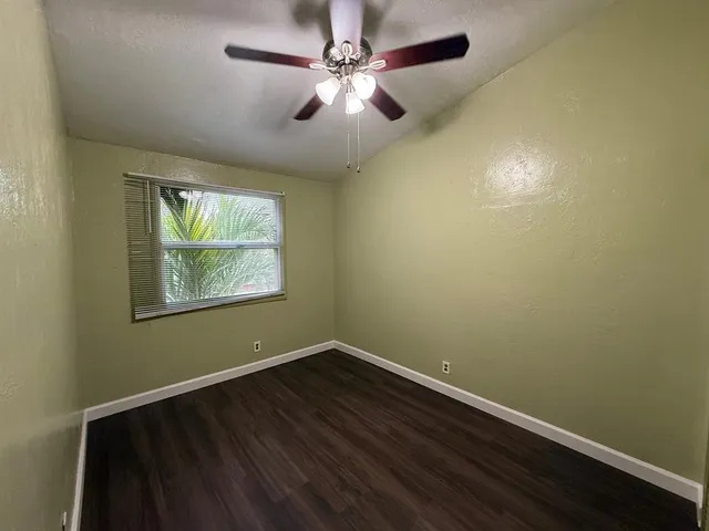 an empty room with wooden floor fan and windows