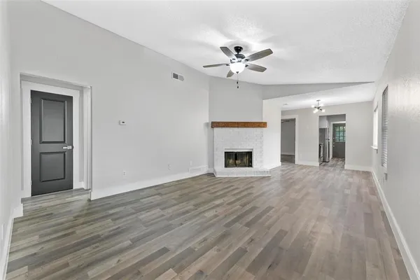 a view of an empty room with wooden floor and a fireplace