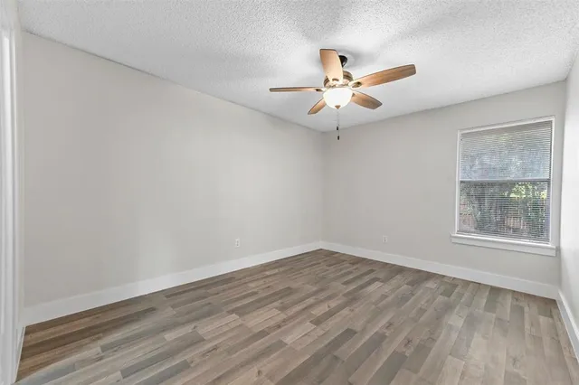 an empty room with wooden floor fan and windows