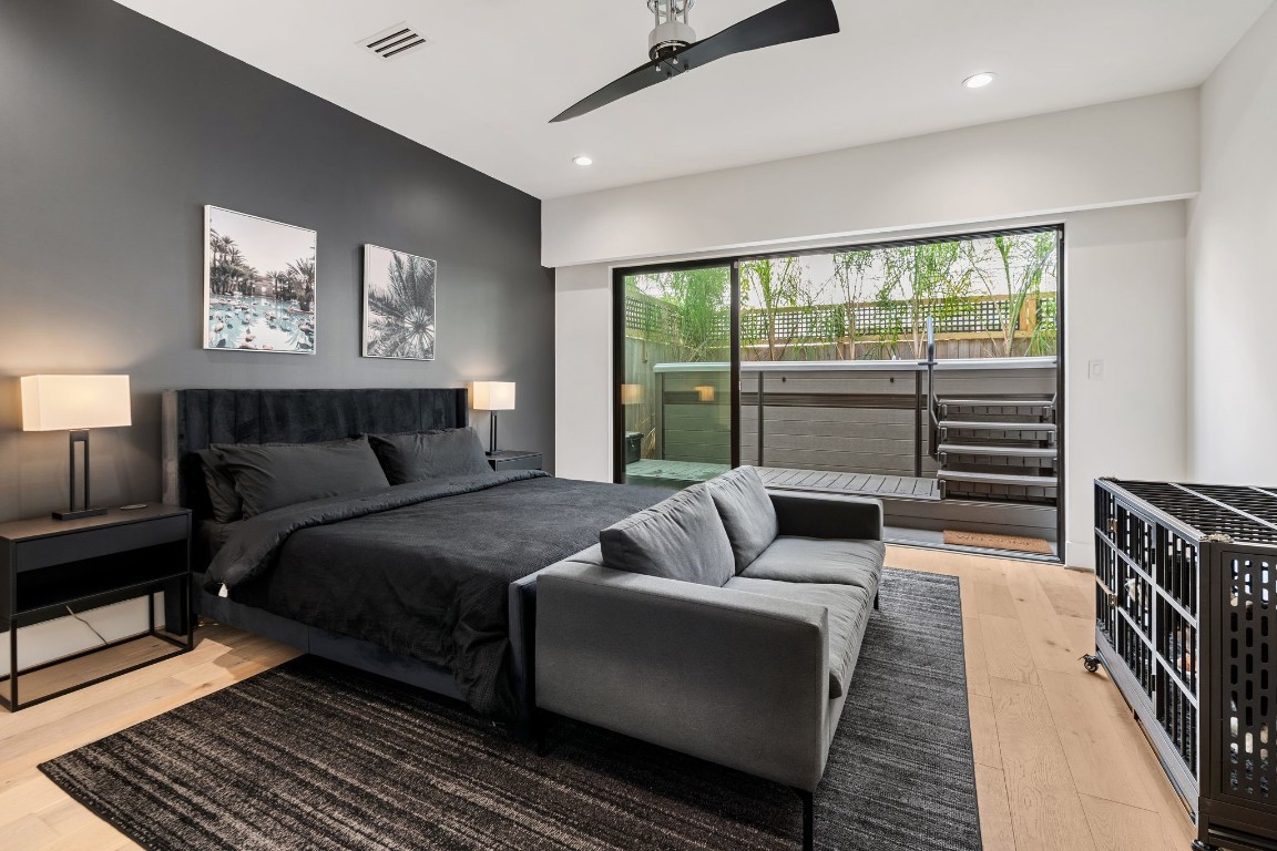 1918 Brun Street Houston, TX 77019 - Photo 6 of 43 A spacious first floor bedroom offers privacy, complete with wide plank wood flooring, a sleek ceiling fan, and a modern accent wall. Expansive sliding glass doors provide direct access to the outdoor living space and hot tub, creating a relaxing retreat with seamless indoor outdoor connectivity.