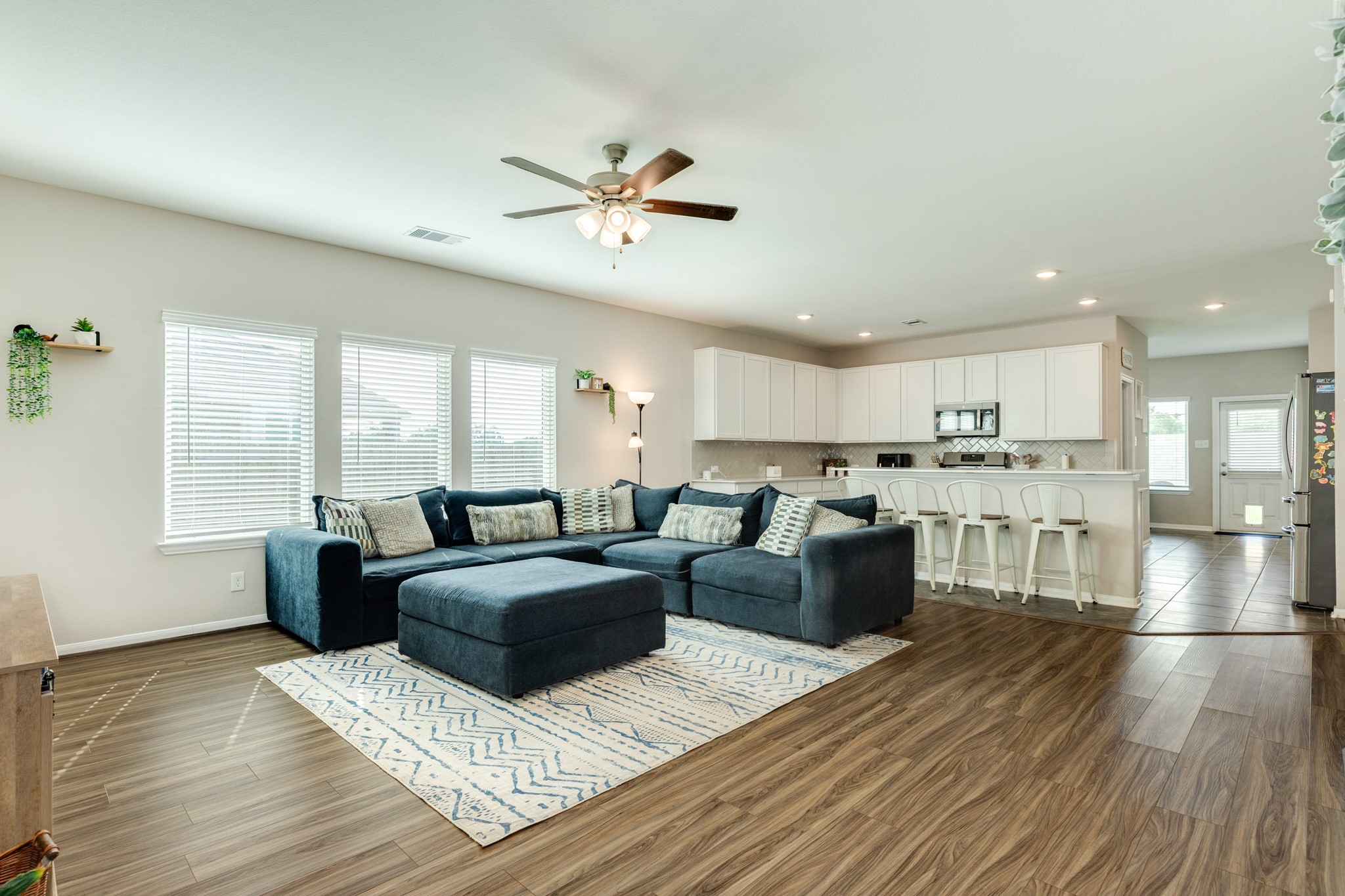 2446 Palisade Crst Drive Rosharon, TX 77583 - Photo 5 of 30 This open-concept living area features a spacious layout with a cozy sectional, large windows for natural light, and a modern kitchen with a breakfast bar. The wood-style flooring adds warmth and elegance to the space.