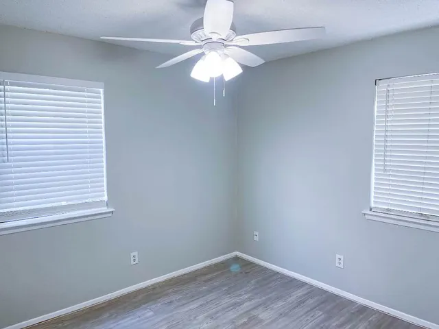 an empty room with wooden floor fan and windows