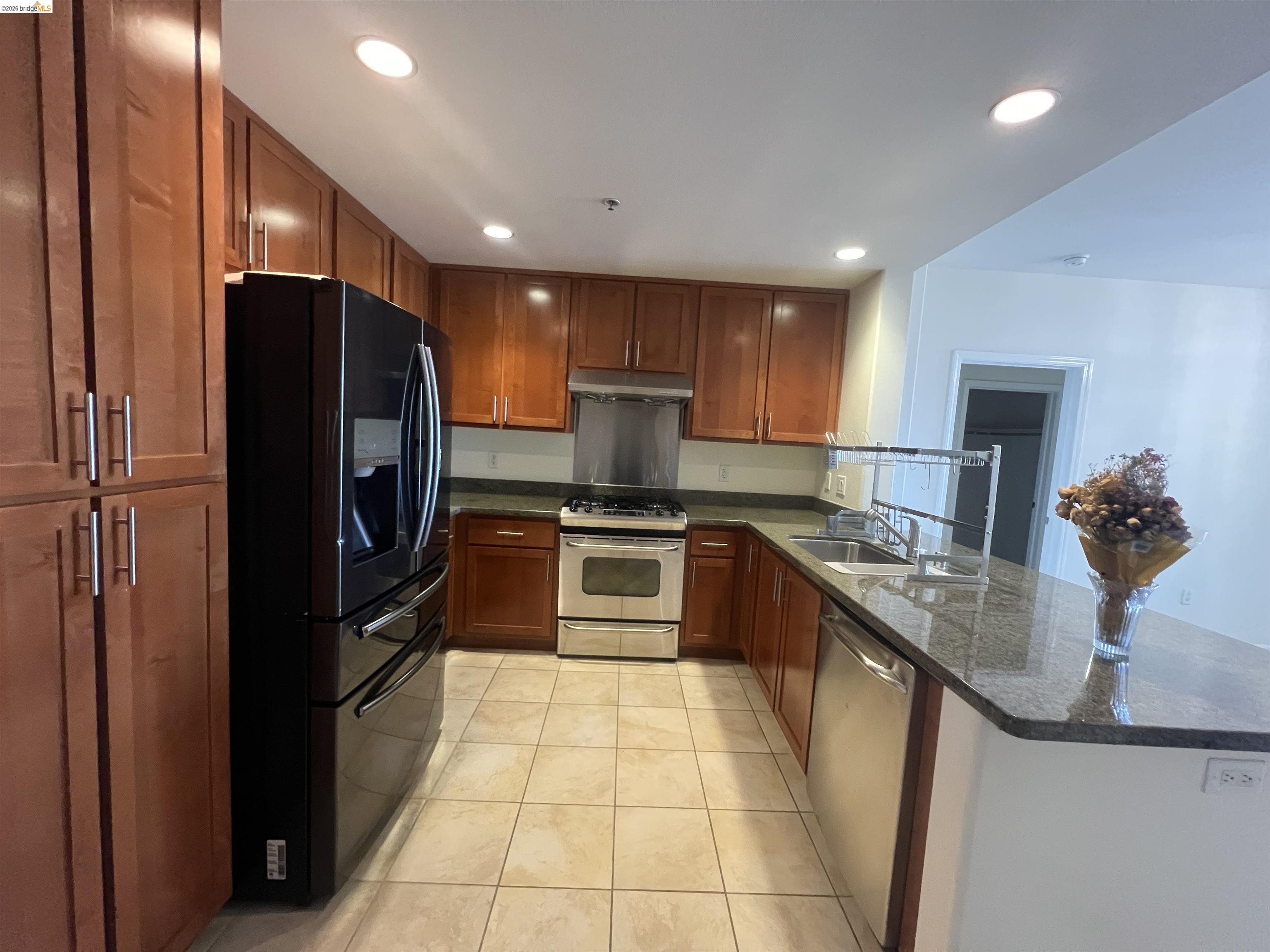 423 7th Street, Unit 313 Oakland, CA 94607 - Photo 3 of 11 Kitchen featuring medium-toned cabinetry, granite-finish countertops, and tile flooring