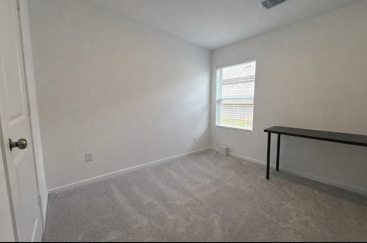 21151 Vercelli Street New Caney, TX 77357 - Photo 13 of 16 Cozy room with neutral walls and carpet, featuring a window that allows natural light. Includes a simple, sleek black table, making it ideal for a home office or study space.