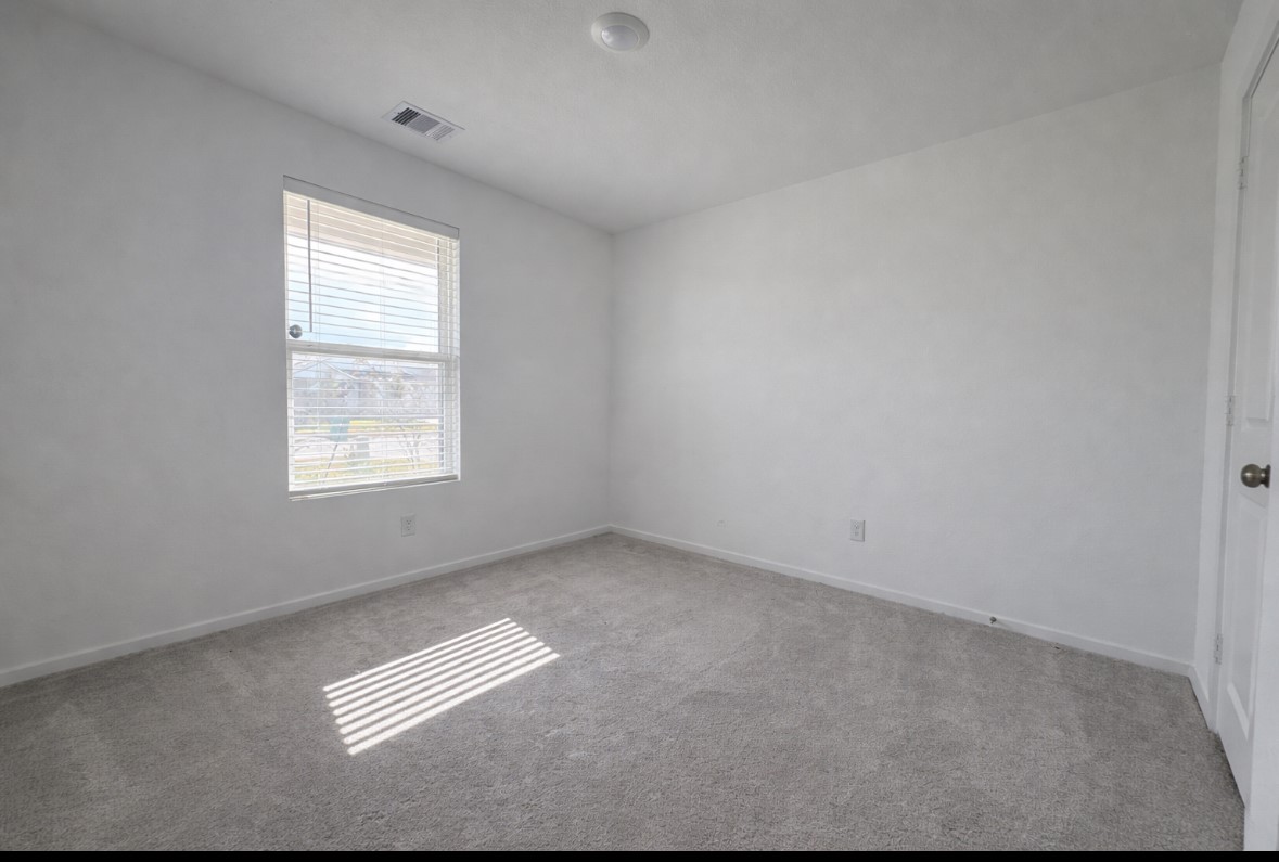 21151 Vercelli Street New Caney, TX 77357 - Photo 14 of 16 This is a bright, empty room with neutral-colored walls and carpet, featuring a window for natural light and a standard door. Ideal for a bedroom or office space.