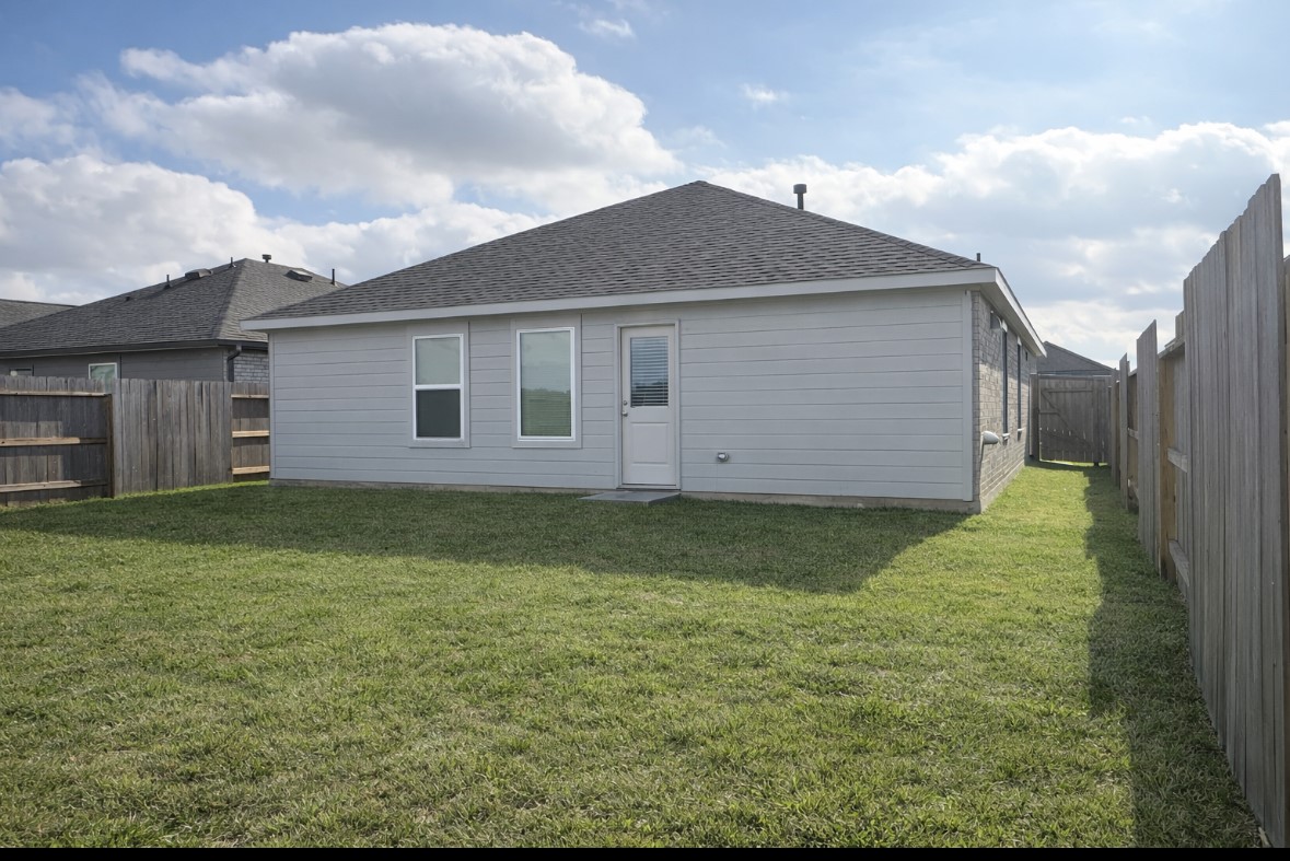 21151 Vercelli Street New Caney, TX 77357 - Photo 16 of 16 A cozy, single-story home with a fenced backyard featuring a well-maintained lawn, perfect for outdoor activities. The exterior is modern with neutral siding and a shingled roof.