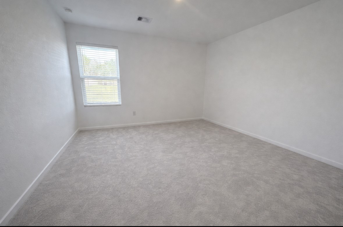 21151 Vercelli Street New Caney, TX 77357 - Photo 8 of 16 This photo showcases a bright, empty room with light-colored carpet and walls, featuring a window that lets in natural light. The space is versatile and ready for personalization.