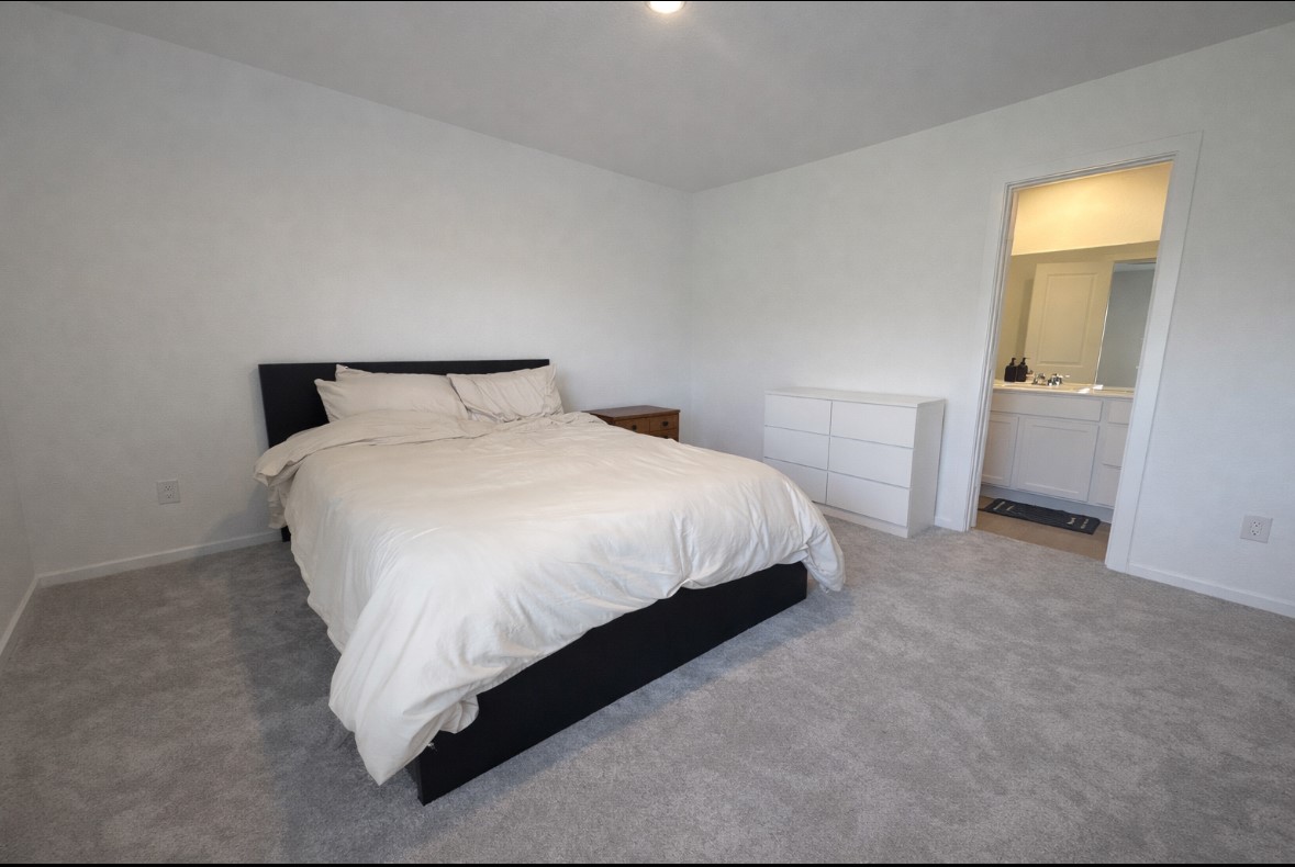 21151 Vercelli Street New Caney, TX 77357 - Photo 9 of 16 This spacious bedroom features a comfortable bed, neutral carpet, and minimalistic decor. It includes a small dresser and connects to a bright en-suite bathroom, offering convenience and privacy.