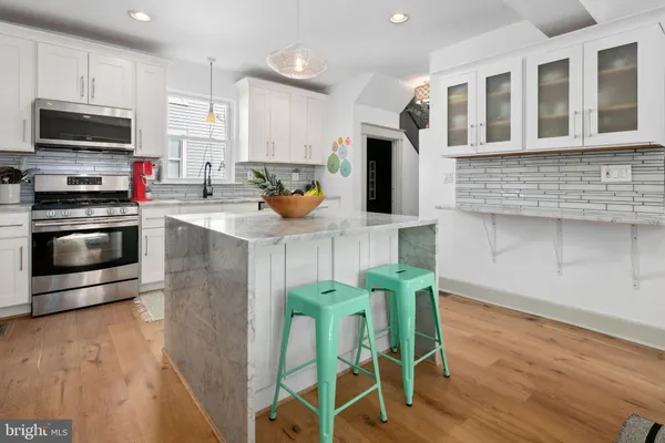 a kitchen with stainless steel appliances granite countertop a stove a microwave a sink a refrigerator white cabinets and wooden floor