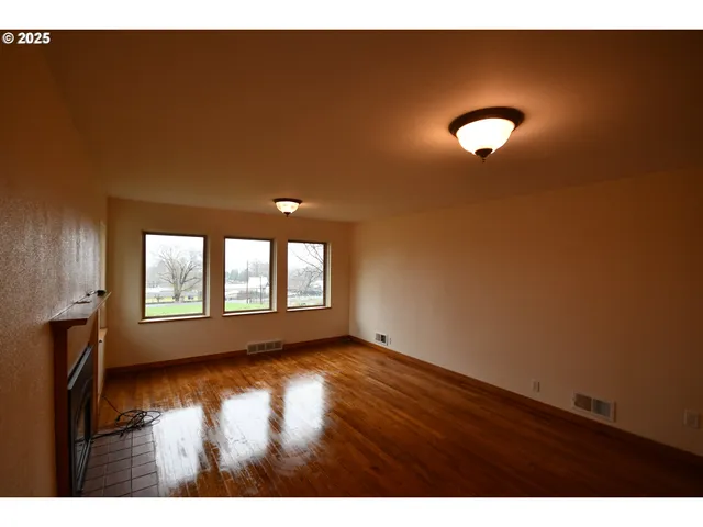 a view of an empty room with a window and wooden floor