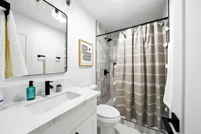 a bathroom with a sink a toilet a shower curtain and a large mirror